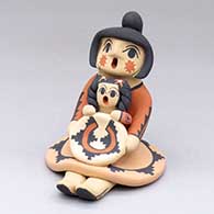 A polychrome sitting grandmother storyteller figure wearing a skirt and holding one child with a welcome basket
 by Chrislyn Fragua of Jemez