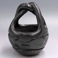 A black engagement basket with a twisted handle and carved with an avanyu design around the body