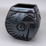 A squarish black-on-black jar carved with multiple figures and geometric designs