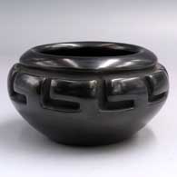 A black bowl carved with a geometric design around the shoulder