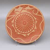 A red plate decorated with a sgraffito avanyu, raincloud, feather ring, and geometric design