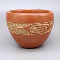 A red bowl decorated around the body with a sgraffito avanyu design