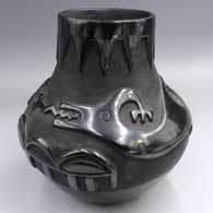 A black jar carved with an avanyu design above the shoulder and a geometric design around the neck