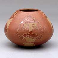 A small red bowl decorated with a four-panel sgraffito kachina, hummingbird, sun, feather and geometric design