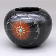 A black bowl with a sgraffito medallion with a sienna spot, an inlaid stone and a ring of feathers design