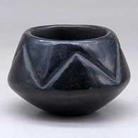 A small black bowl carved with a geometric design above the shoulder
 by Juanita Gonzales of San Ildefonso