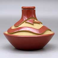 A low shouldered red jar with a thin neck and carved above the shoulder with an avanyu design, click or tap to see a larger version