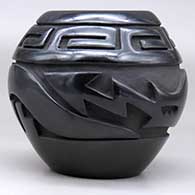 A black jar carved around the body with an avanyu  and scrolls design, click or tap to see a larger version