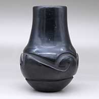 A black jar with a tall neck and carved around the shoulder with a geometric design, click or tap to see a larger version