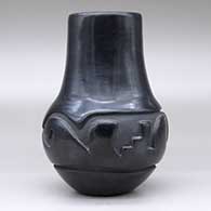 A black jar with a tall neck and carved around the shoulder with a geometric design, click or tap to see a larger version