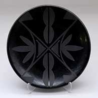 A black on black plate decorated on top with a four panel geometric design
 by Maria Martinez of San Ildefonso