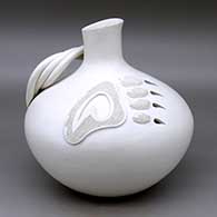 A large white seed pot jar with a short neck, a three strand handle, and a bear paw applique with sgraffito design and cutouts
 by Stella Shutiva of Acoma