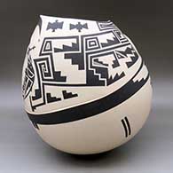 A large black on beige jar with a kiva step cut organic opening and a lightly carved and painted serpent, fish and geometric design, click or tap to see a larger version
