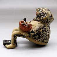 A backward leaning sitting shaman figure holding a knife, a bowl with ears of corn and with a metate between his feet, click or tap to see a larger version