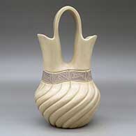 A beige wedding vase with a swirl melon-carved body and a band of black on beige scrolls geometric design around the neck, click or tap to see a larger version