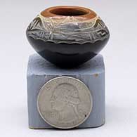 A miniature black seed pot with a sienna rim and a sgraffito avanyu, feather and geometric design above the shoulder
 by Geri Naranjo of Santa Clara