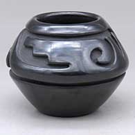 A small black bowl carved with a stylized avanyu design above the shoulder
 by Stella Chavarria of Santa Clara