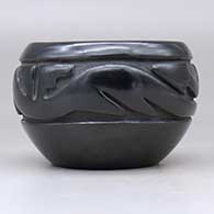 A black bowl with a carved avanyu design around the body, click or tap to see a larger version
