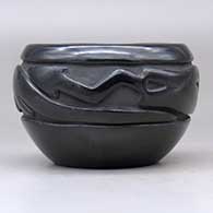 A black bowl with a carved avanyu design around the body, click or tap to see a larger version