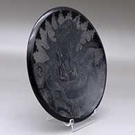 A black plate decorated with a sgraffito serpent, nature scene, kiva step and geometric design, click or tap to see a larger version