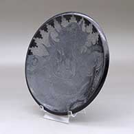 A black plate decorated with a sgraffito serpent, nature scene, kiva step and geometric design, click or tap to see a larger version