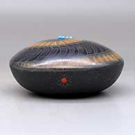 A black seed pot with a black micaceous base and a sienna spiral in a sgraffito feather and geometric design, plus five inlaid stones, click or tap to see a larger version