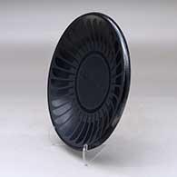 A black on black plate decorated with a ring of feathers and crosshatching design, click or tap to see a larger version