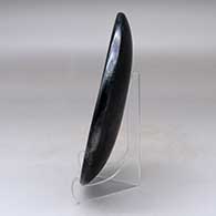 A black on black plate decorated with a ring of feathers and crosshatching design, click or tap to see a larger version
