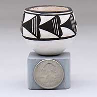 A miniature black-on-white bowl decorated with an eight-panel rain cloud geometric design above the shoulder
 by Lucy Lewis of Acoma