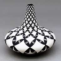 A black on white tear drop jar with a long neck and decorated with a pumpkin seed snowflake and geometric design
 by Dorothy Torivio of Acoma