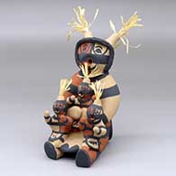 A sitting koshare storyteller figure with three children and corn husks
 by Janeth Fragua of Jemez