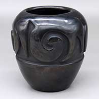 A black jar with sienna spots, carved with a stylized avanyu design around the shoulder
 by Mela Youngblood of Santa Clara
