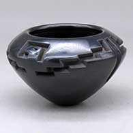 A small black bowl carved around the shoulder with a four panel eagle, kiva step and geometric design
 by Effie Garcia of Santa Clara