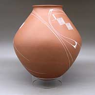 A white on red jar with a recurved lip and decorated with a flowing geometric design, click or tap to see a larger version