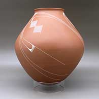 A white on red jar with a recurved lip and decorated with a flowing geometric design, click or tap to see a larger version