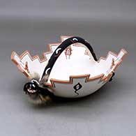 A polychrome Zuni prayer bowl decorated inside with frog appliques and geometric design, and outside with tadpoles and geometric design with a kolowisi handle decorated with a face, horn, headdress, geometric design, string and feathers
 by Marcus Homer of Zuni