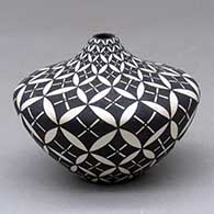 A small black on white tear drop jar decorated with a pumpkin seed snowflake and geometric design
 by Dorothy Torivio of Acoma