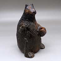 A standing brown bear holding a jar coin bank 
 by Louise Goodman of Dineh