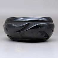 An oval black bowl polished inside and carved around the outside with an avanyu and geometric design, click or tap to see a larger version