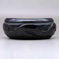 An oval black bowl polished inside and carved around the outside with an avanyu and geometric design, click or tap to see a larger version