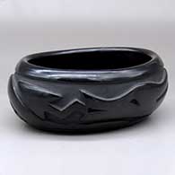 An oval black bowl polished inside and carved around the outside with an avanyu and geometric design
 by Pablita Chavarria of Santa Clara
