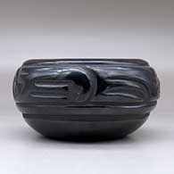 A black bowl carved with a stylized avanyu design around the body, click or tap to see a larger version