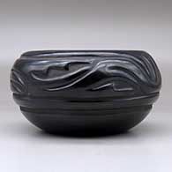 A black bowl carved with a stylized avanyu design around the body, click or tap to see a larger version