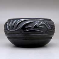A black bowl carved with a stylized avanyu design around the body, click or tap to see a larger version