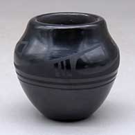 A small black on black jar decorated with a four panel geometric design around the shoulder
 by Helen Gutierrez of San Ildefonso
