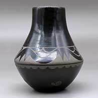 A black on black jar decorated with an avanyu, cloud, spider and geometric design, plus an inlaid stone, click or tap to see a larger version