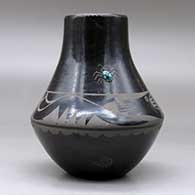 A black on black jar decorated with an avanyu, cloud, spider and geometric design, plus an inlaid stone, click or tap to see a larger version