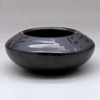A small black on black bowl decorated with a four-panel bat wing and geometric design above the shoulder
 by Blue Corn of San Ildefonso