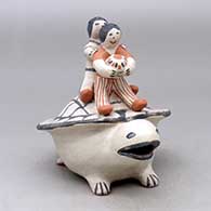 Two children sitting on the shell of a turtle figure
 by Seferina Ortiz of Cochiti