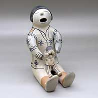 A sitting grandfather storyteller figure with one child
 by Helen Cordero of Cochiti
